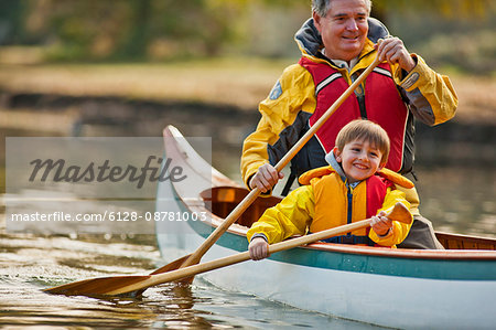 Happy grandfather and young grandson canoeing together on a lake.