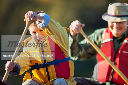 Happy grandfather and young grandson canoeing together on a lake.