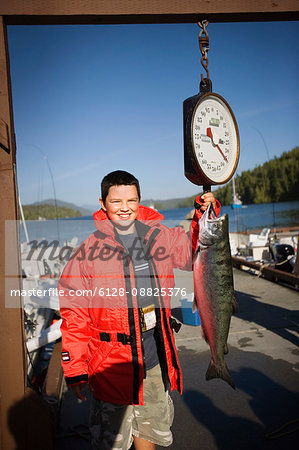 Portrait of a smiling boy weighing a fish he has caught.