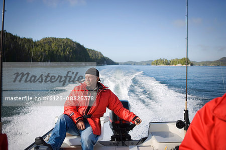 Mature man steering a motor at the rear of a boat.