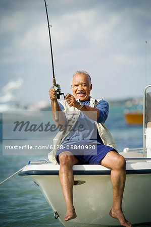 Smiling mature man fishing off the side of a boat in the ocean