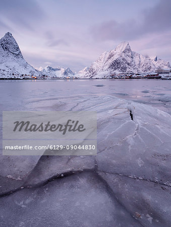 The frozen sea and the snowy peaks frame the fishing village at sunset Reine Nordland Lofoten Islands Norway Europe