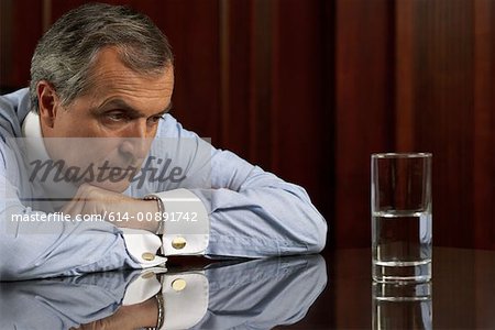 Businessman looking pessimistically at a glass of water