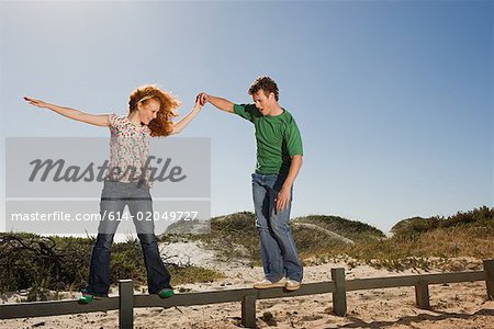 A young man helping a woman balancing on a fence
