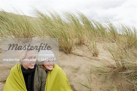 Women sharing a blanket on dune