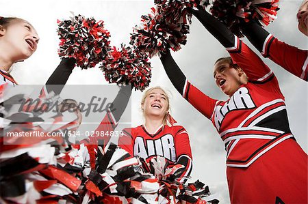 Cheerleaders doing routine with pom poms on football field, Stock