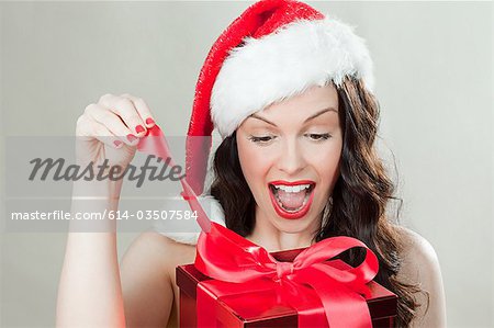 Young brunette woman wearing Santa hat opening Christmas present
