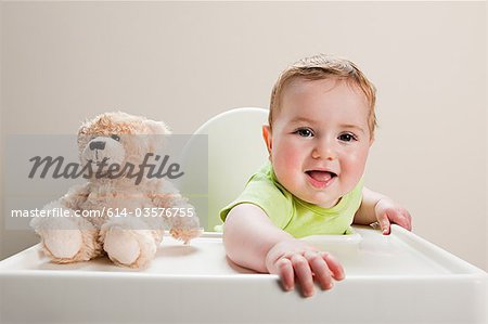 Baby boy sitting in highchair with teddy bear