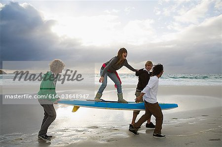 Young people carrying surfboard, person balancing on top