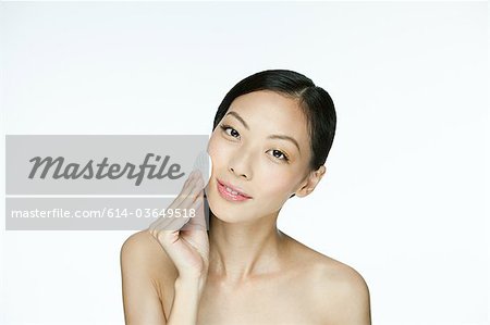 Young woman using cotton pad on face