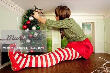 Young woman in small room decorating christmas tree Young woman in small room decorating christmas tree