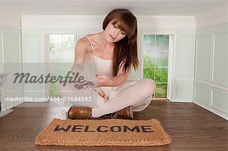 Young woman in small room with key and welcome mat Young woman in small room with key and welcome mat