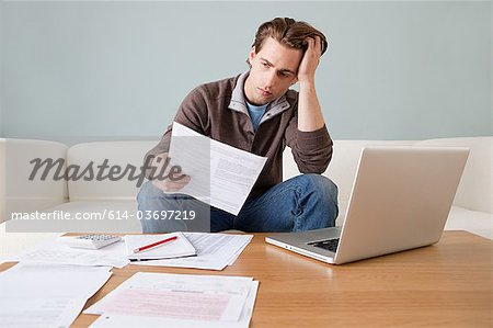 Worried young man with paperwork using laptop