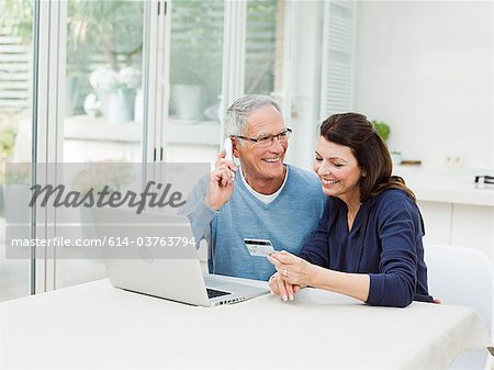 Mature couple using laptop, man on telephone