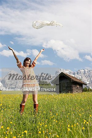Woman throwing scarf in meadow with Bavarian Alps in background, Germany