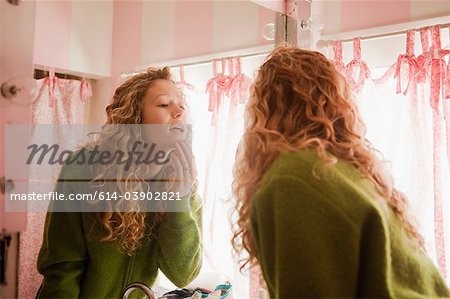 Teenage girl checking skin in bathroom mirror