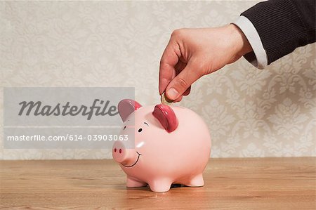 Man inserting pound coin into piggy bank