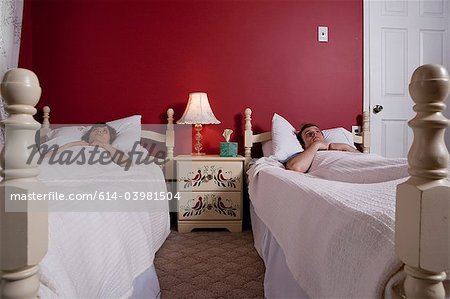 Young couple lying awake in single beds