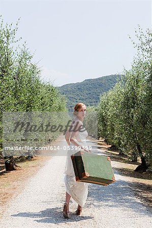 Bride carrying suitcase on country road