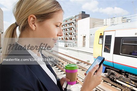 Businesswoman with coffee and smart phone in train station