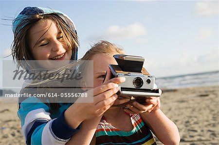 Girl showing friend how to use instant camera at beach