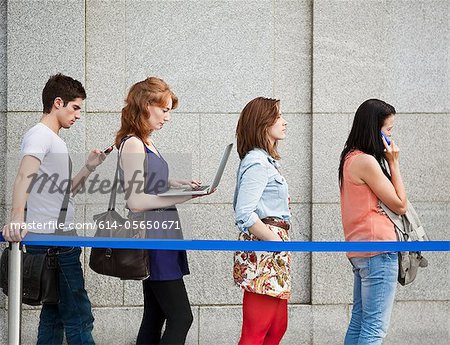 Four people in a queue, one using a laptop Four people in a queue, one using a laptop