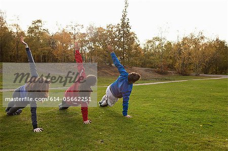 Three young friends stretching on grass in park