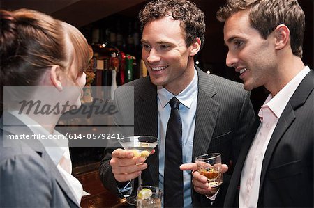 Two buisnessmen chatting to female colleague at bar