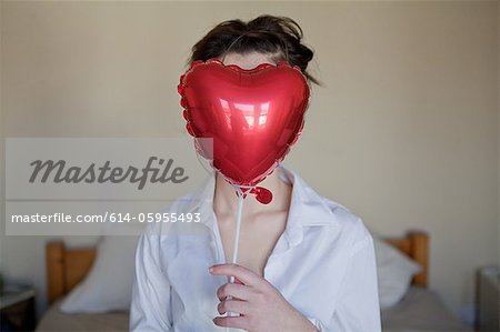 Young woman with heart shaped balloon in front of her face