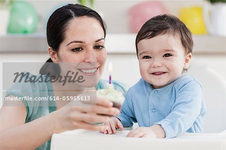 Mother giving birthday cupcake to baby son