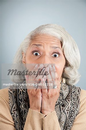 Portrait of senior woman covering mouth with hands in studio