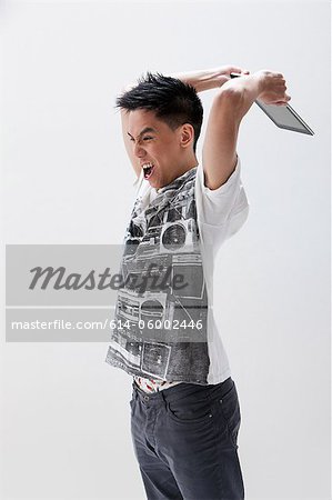Young Asian man about to break digital tablet, studio shot