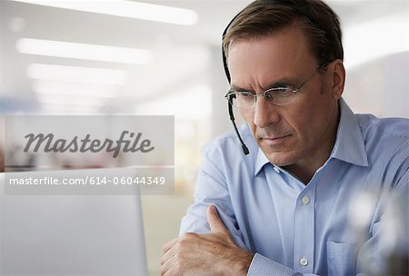 Mature businessman wearing headset and using laptop