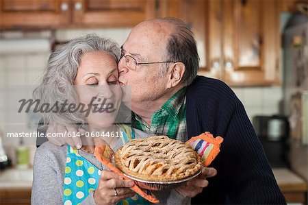 Senior man kissing woman holding freshly baked pie