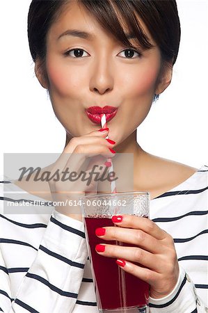 Young woman drinking from straw against white background