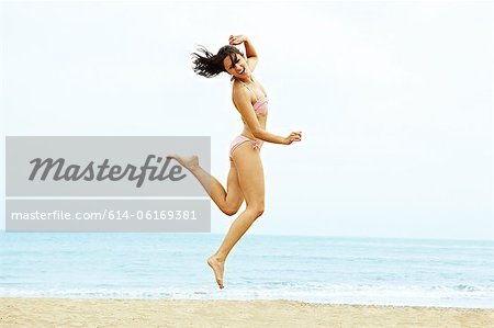 Young woman in bikini jumping on beach