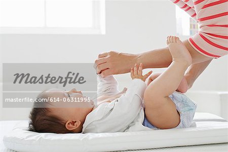 Mother changing baby girl on mat