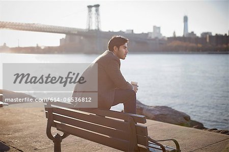 Man with cup of coffee on park bench