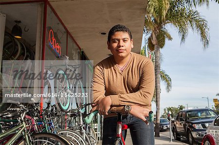 Boy leaning on bicycle outside shop