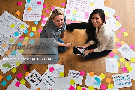 Colleagues sitting on floor with digital tablet, papers and adhesive notes