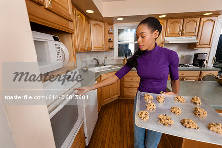 Woman putting tray of cookies into oven