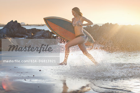 Young woman with surfboard running on beach