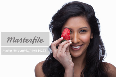 Young woman covering eye with strawberry