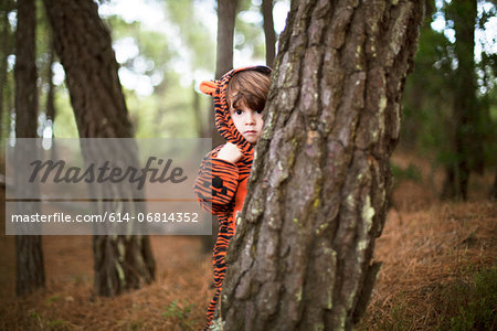 Male toddler wearing tiger suit hiding behind tree