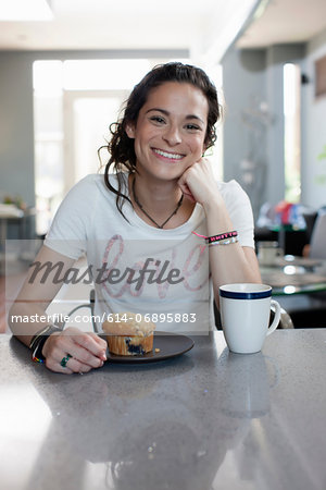 Young woman enjoying coffee and muffin in kitchen, portrait