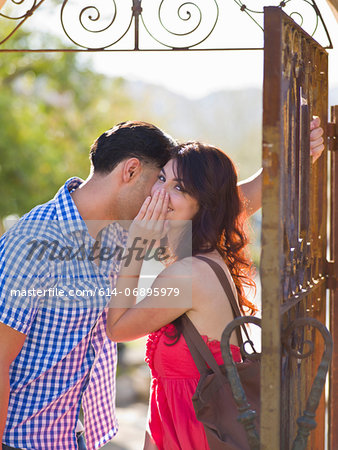 Young woman whispering to man by iron gate, portrait