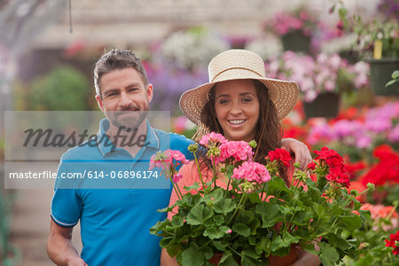 Mid adult man and young woman holding plants in garden centre, portrait