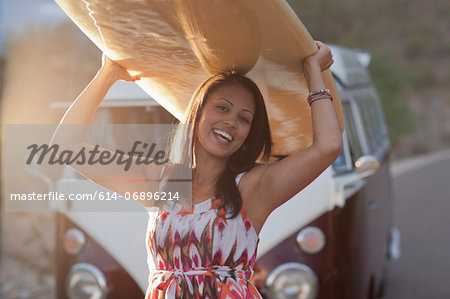 Young woman holding surfboard on road trip, smiling