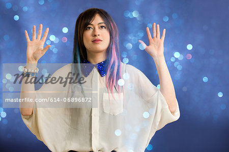Portrait of young woman with arms up looking at glitter