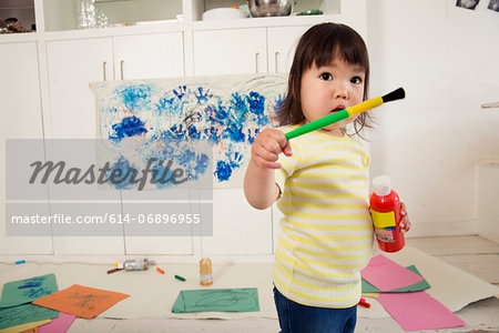 Female toddler holding paint bottle and brush